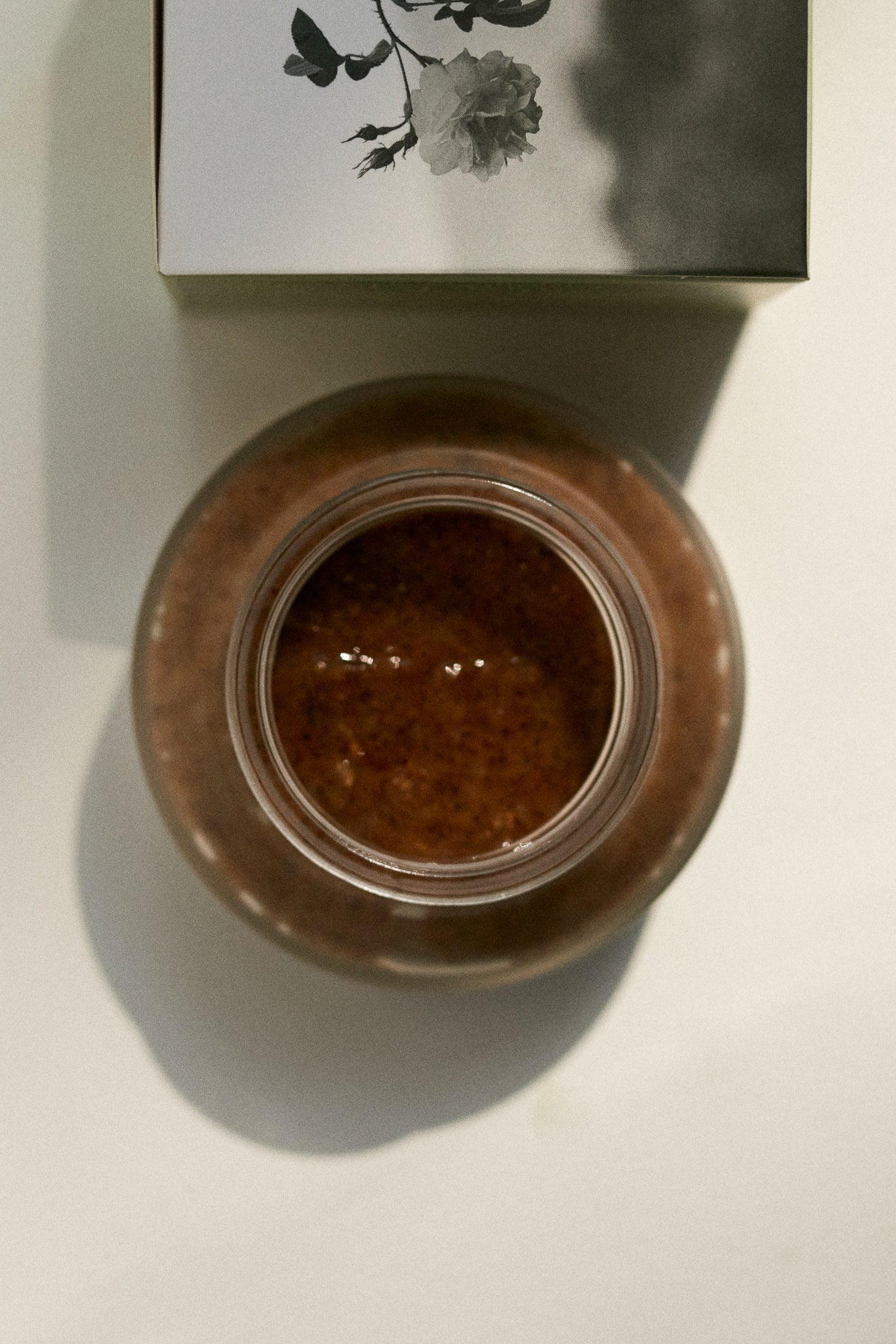 Aerial view of the Wild Rose & Geranium Illuminating Exfoliant by Fields of Yarrow jar with the lid open showing the product